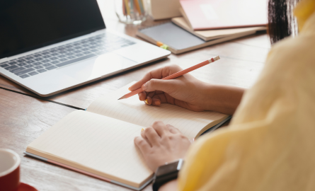 Student writing in a notebook and looking at a laptop